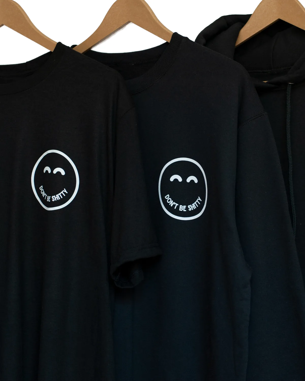 Black DON'T BE SHITTY smiley t-shirt, crewneck and hoodie hanging together