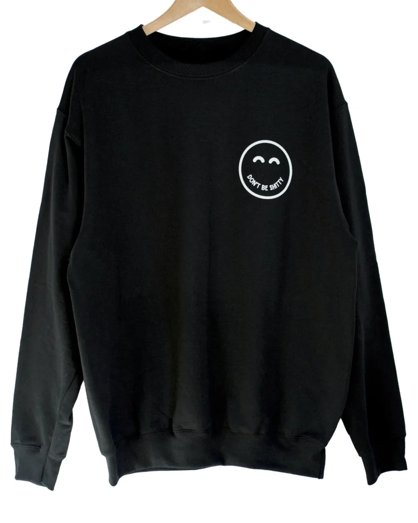 Black DON'T BE SHITTY smiley crewneck sweatshirt on a hanger