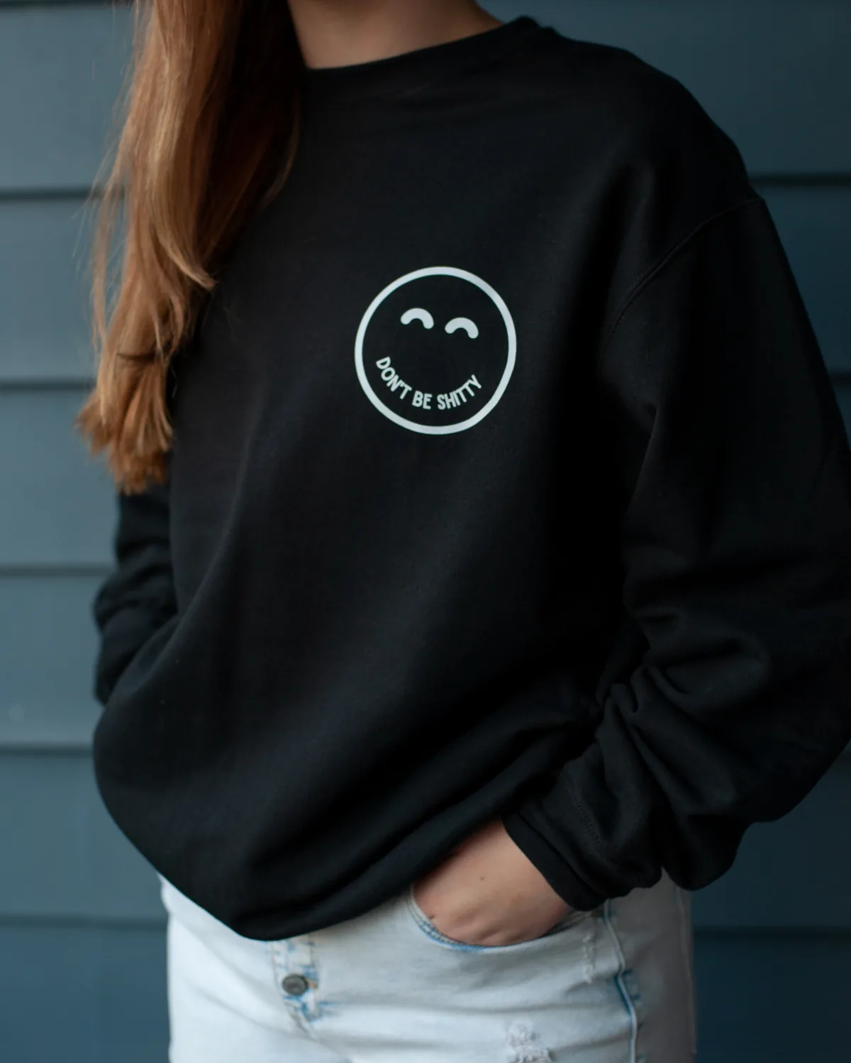 Woman wearing the black DON'T BE SHITTY smiley crewneck sweatshirt