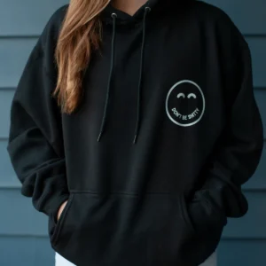 dbs-smiley-hoodie-black-worn-front Woman wearing the black DON'T BE SHITTY smiley hoodie with her hands in the front pouch pocket