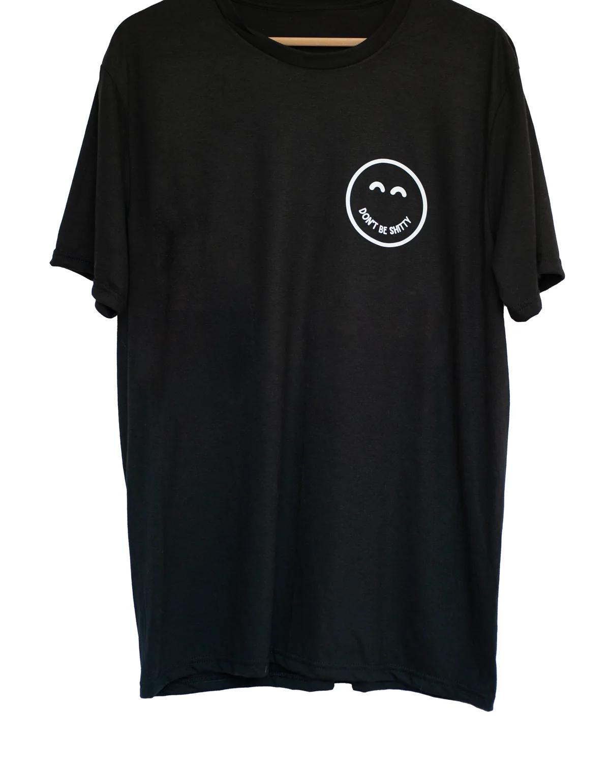 Black DON'T BE SHITTY smiley t-shirt on a hanger, small smiley logo on the left chest