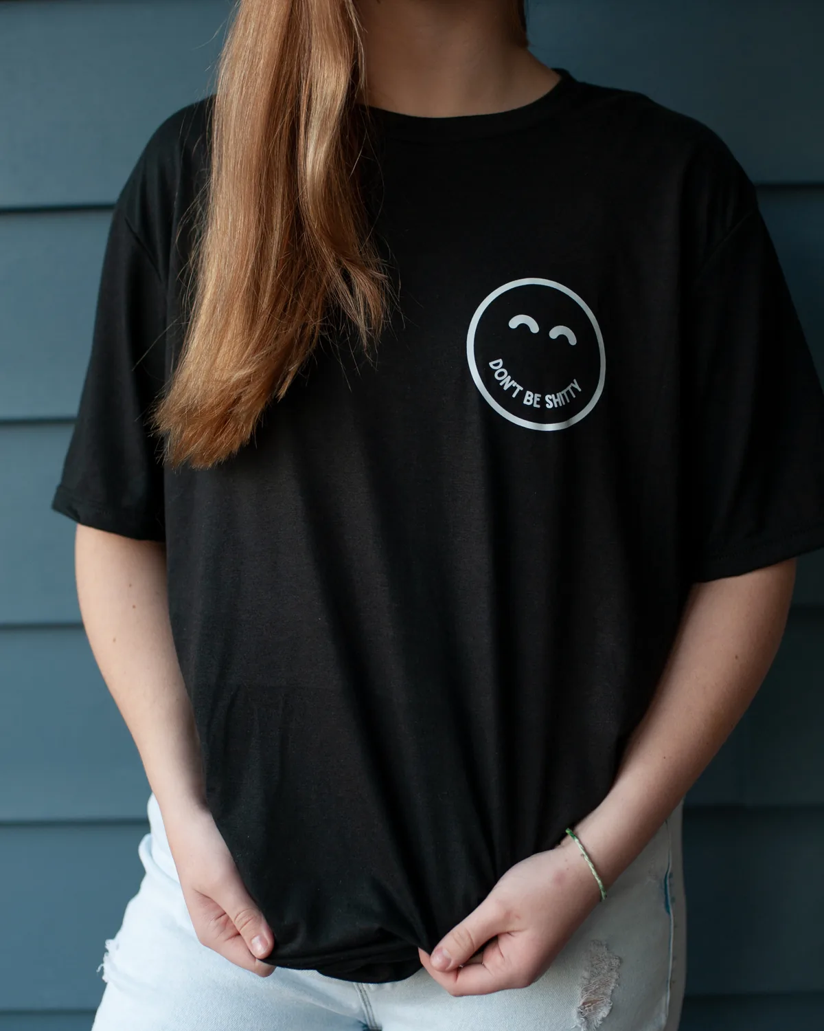 Woman wearing the black DON'T BE SHITTY smiley t-shirt